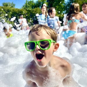 a kid wearing green glasses smiling at a foam party