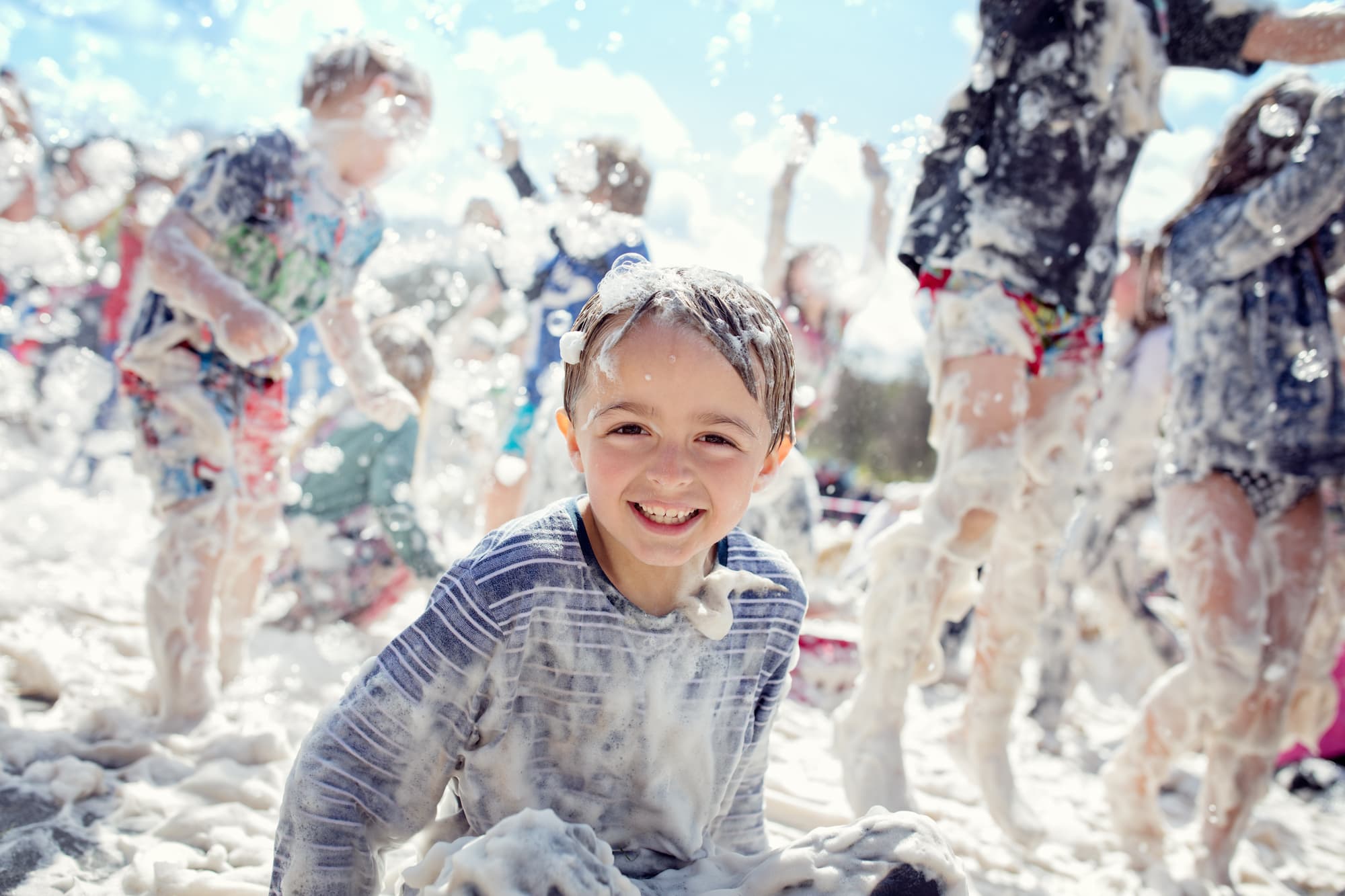 Kid smiling and laughing covered in soap suds at a foam party