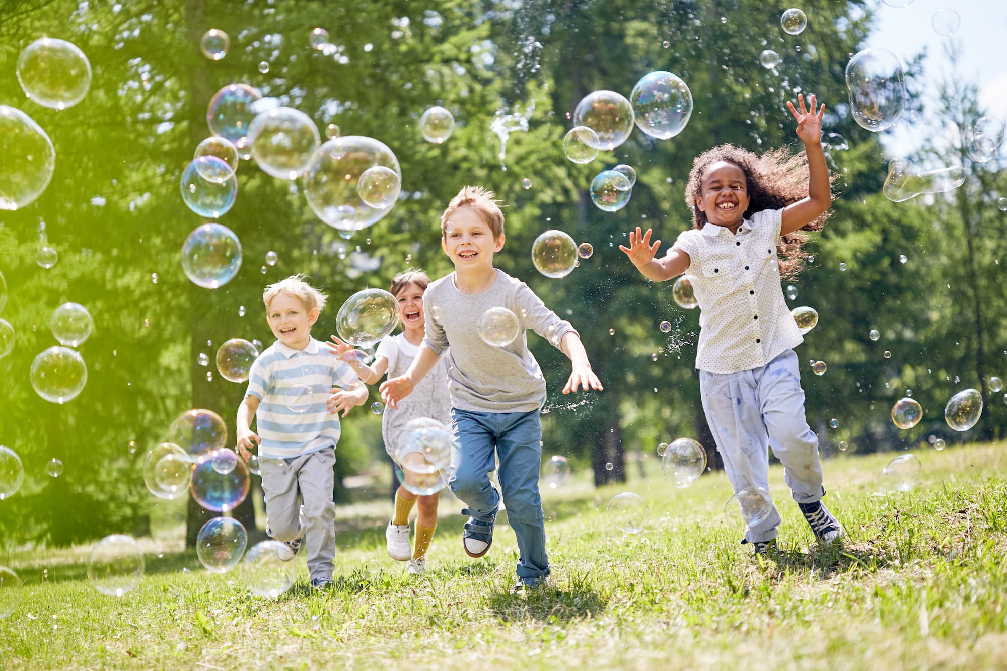 group of little friends with toothy smiles on their faces enjoying warm sunny day while playing in a soap bubbles show